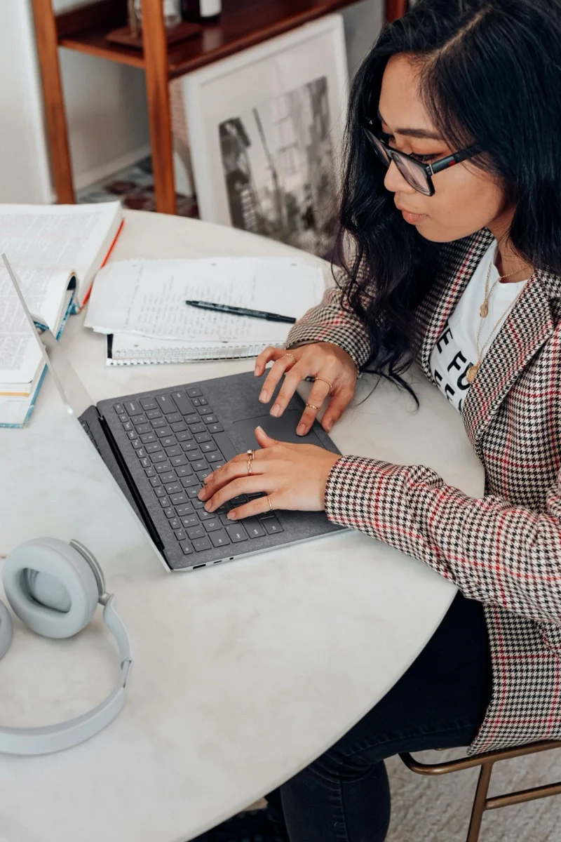 Woman typing on a laptop at a desk with books and headphones